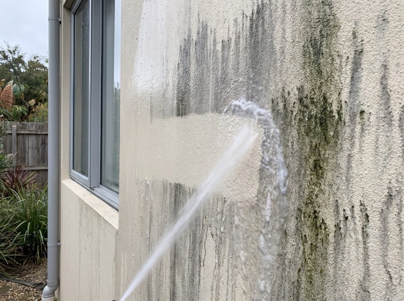 A rendered exterior wall being washed down beside a window