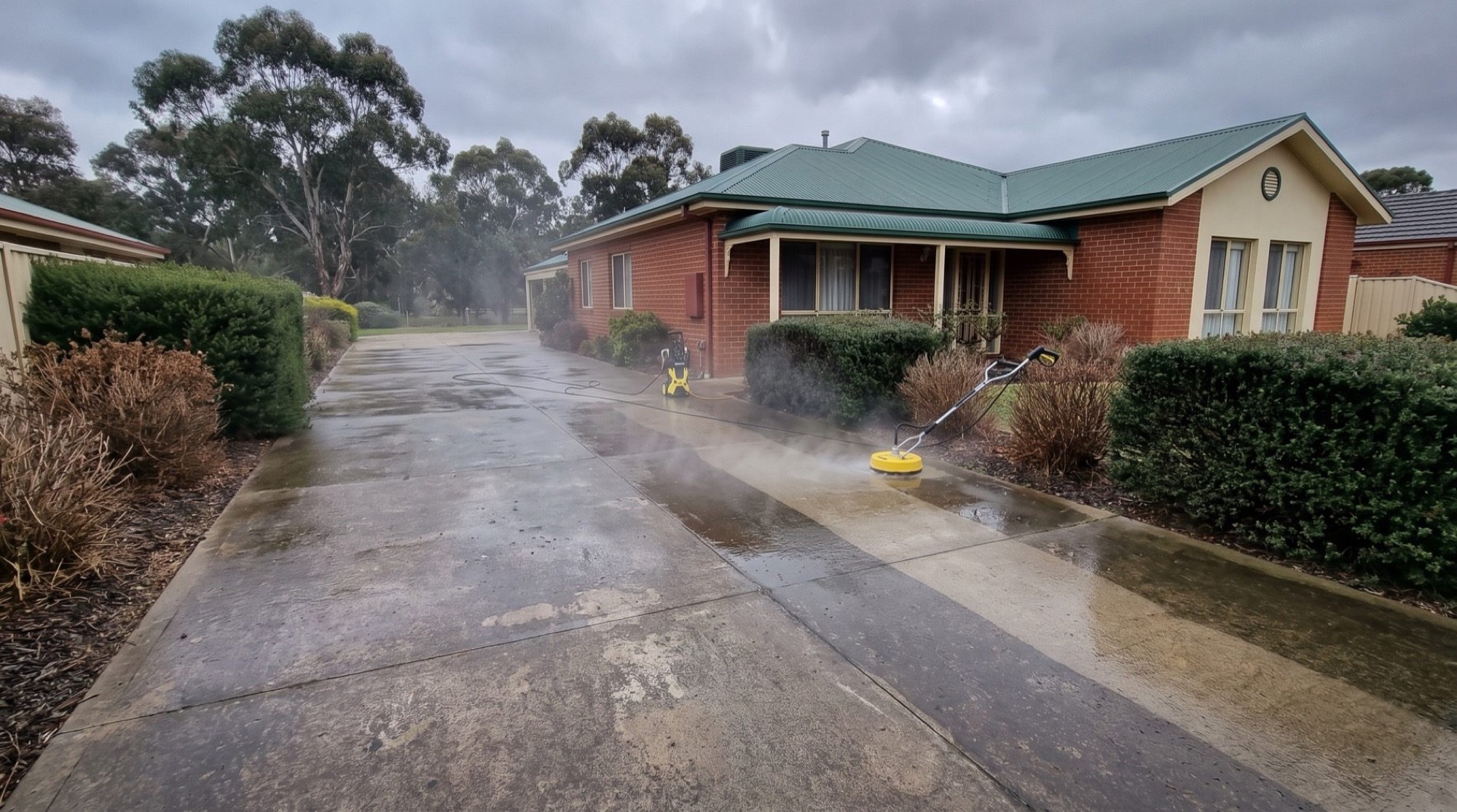 A brick home with a freshly washed driveway under gum trees