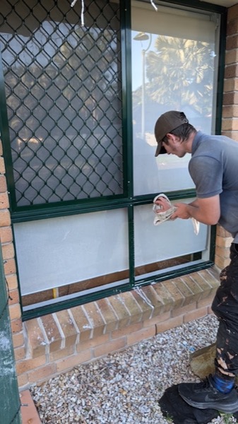 A Shine Exterior team member wiping down an exterior window pane beside a security screen