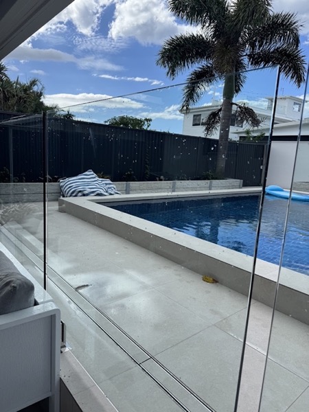 A frameless glass pool fence beside a tiled pool surround