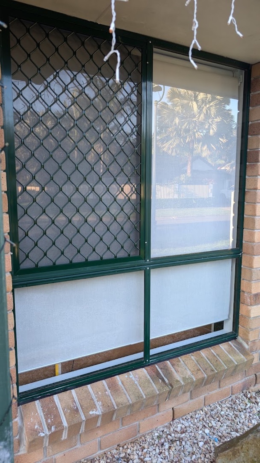 A green-framed window and security screen on a brick wall
