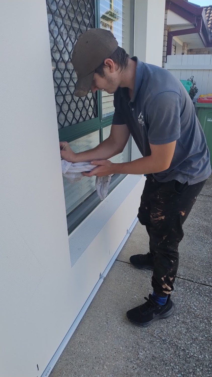 A Shine Exterior team member cleaning a window on a white weatherboard wall